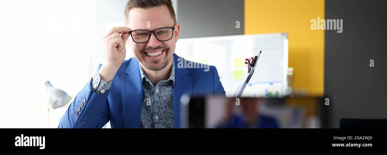 Businessman smiling and adjusting glasses in front of mobile phone ...