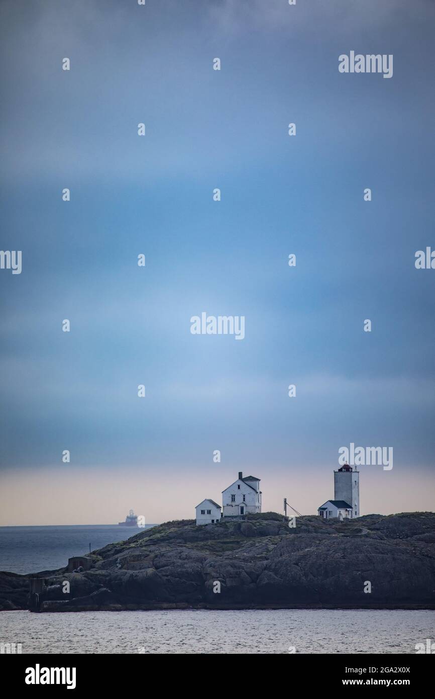 Terningen Lighthouse at twilight on a remote island in the Municipality of Hitra near the mouth of the Hemnfjorden with a ship on the horizon in th... Stock Photo