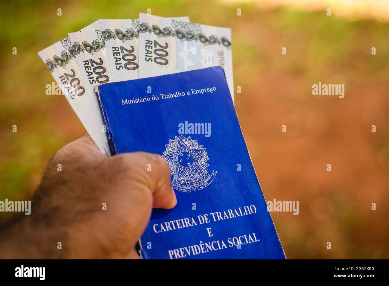 In this photo illustration, a man displays his Work and Social Security Card of Brazil with two hundred reals bills.It is the document that guarantees access to the rights of the Brazilian worker. Stock Photo