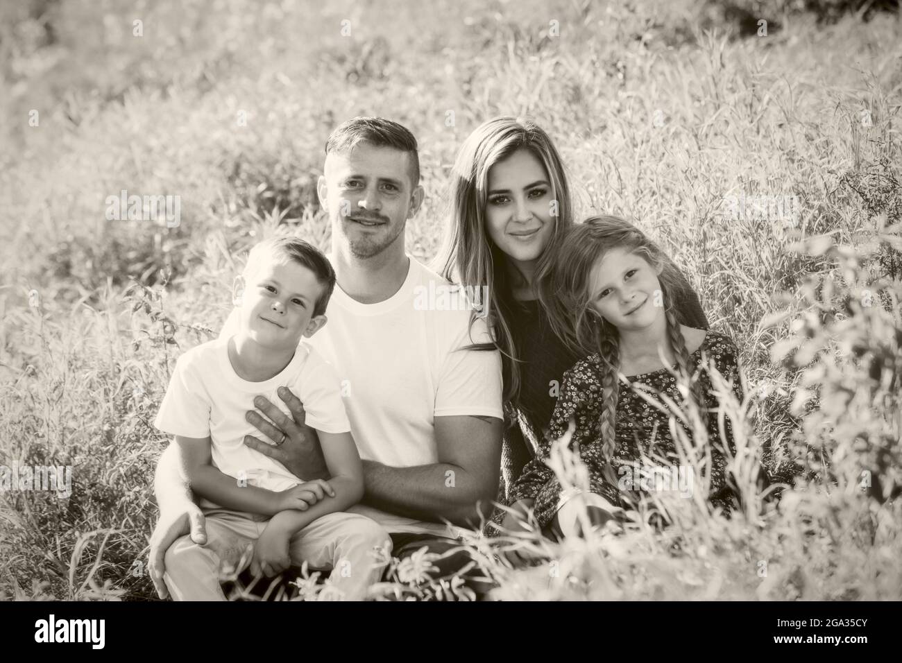 Black and white portrait of a family of four with two young children sitting on grass in a park; Edmonton, Alberta, Canada Stock Photo