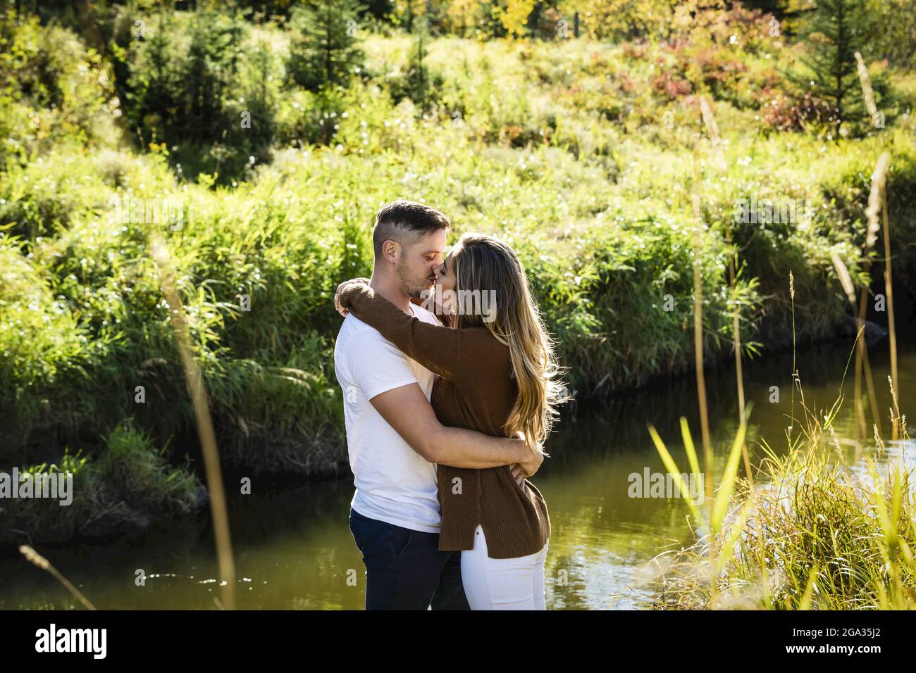 Husband and wife spending quality time together and kissing outdoors near a stream in a city park; Edmonton, Alberta, Canada Stock Photo