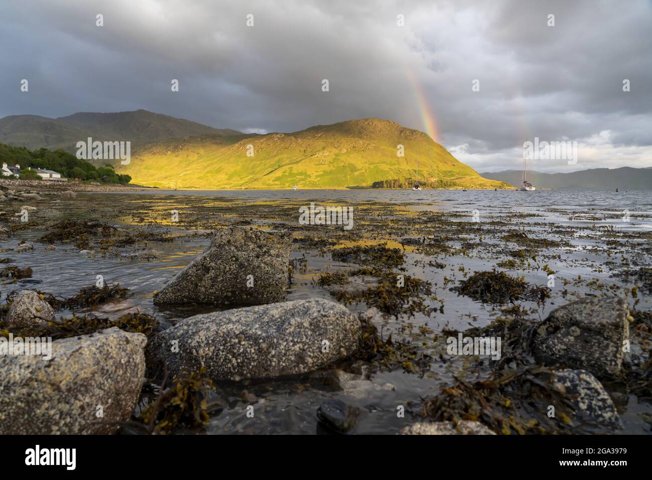 A rainbow spans the sky over Loch Nevis near the rocky shoreline of Inverie, Scotland; Inverie, Scotland Stock Photo