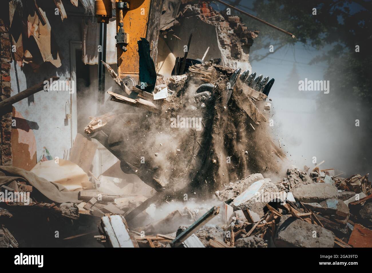 Excavator bucket lifts debris from demolished house, sand and dust pouring, house destruction. Stock Photo