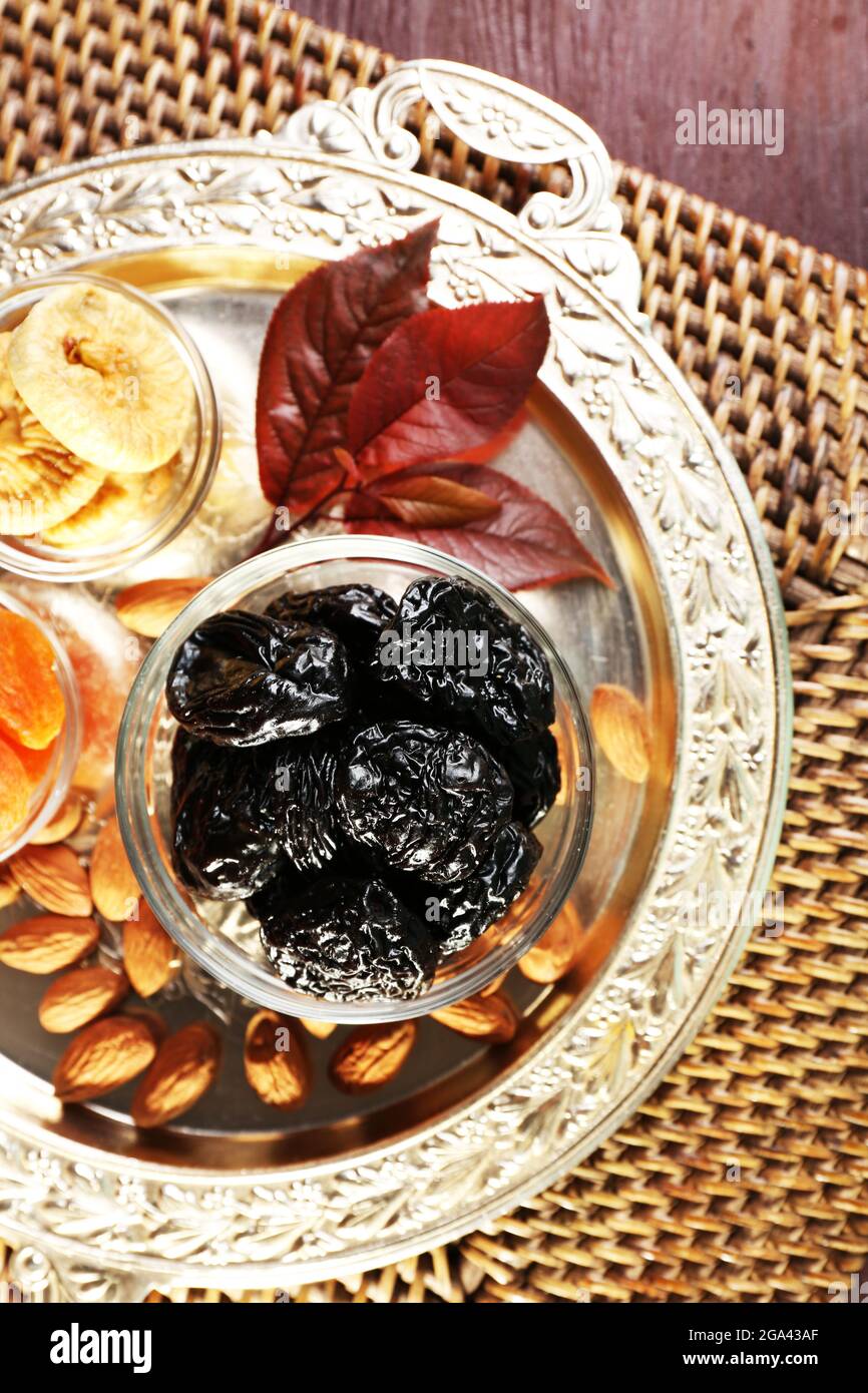 Prunes and other dried fruits in glass saucers with grape leaves on metal tray and wicker mat