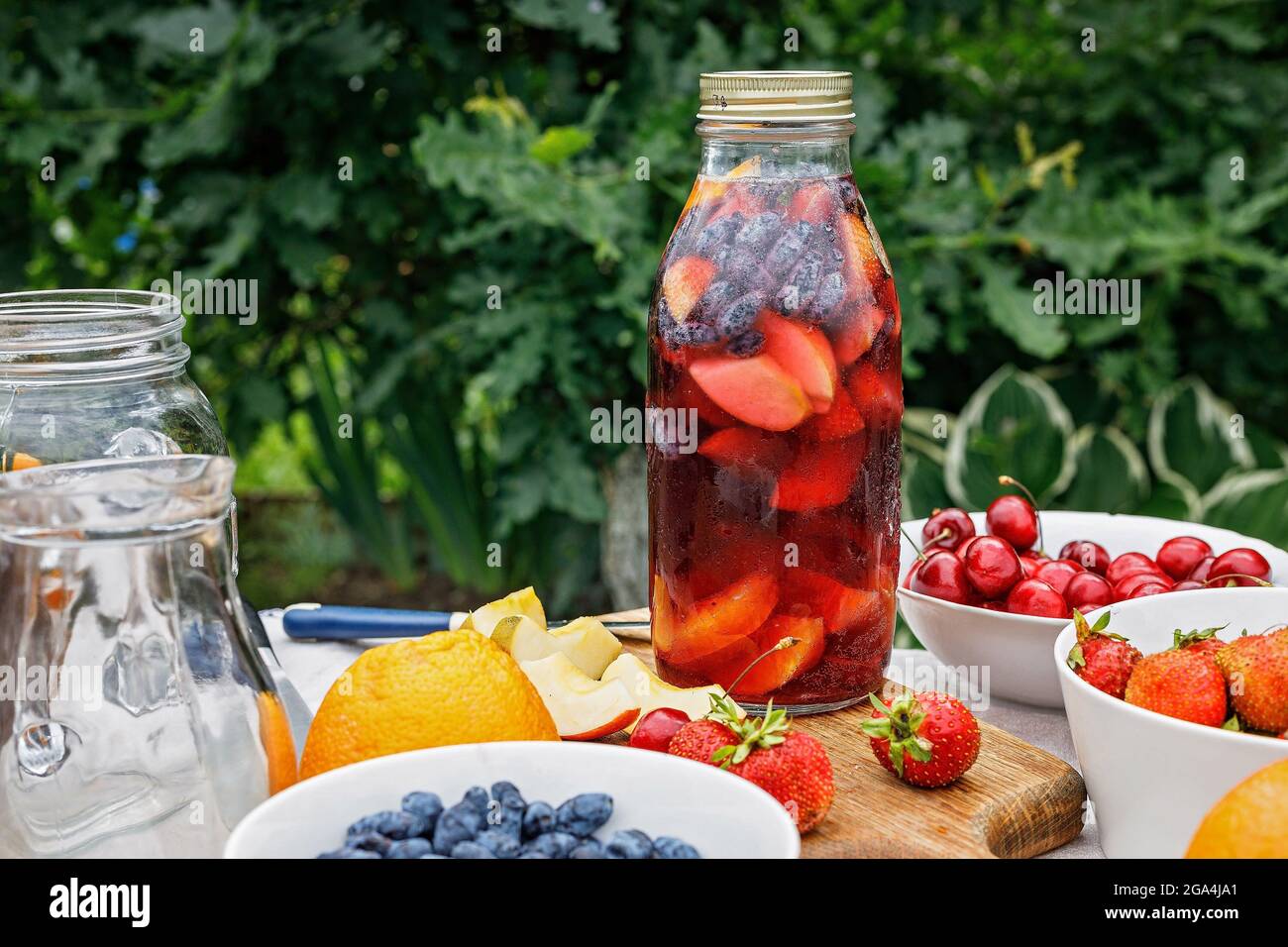 Punch made from organic fruits and berries. Refreshing alcohol-free summer drink with ice and fruit juice. Homemade drink in a glass bottle. Apples, s Stock Photo
