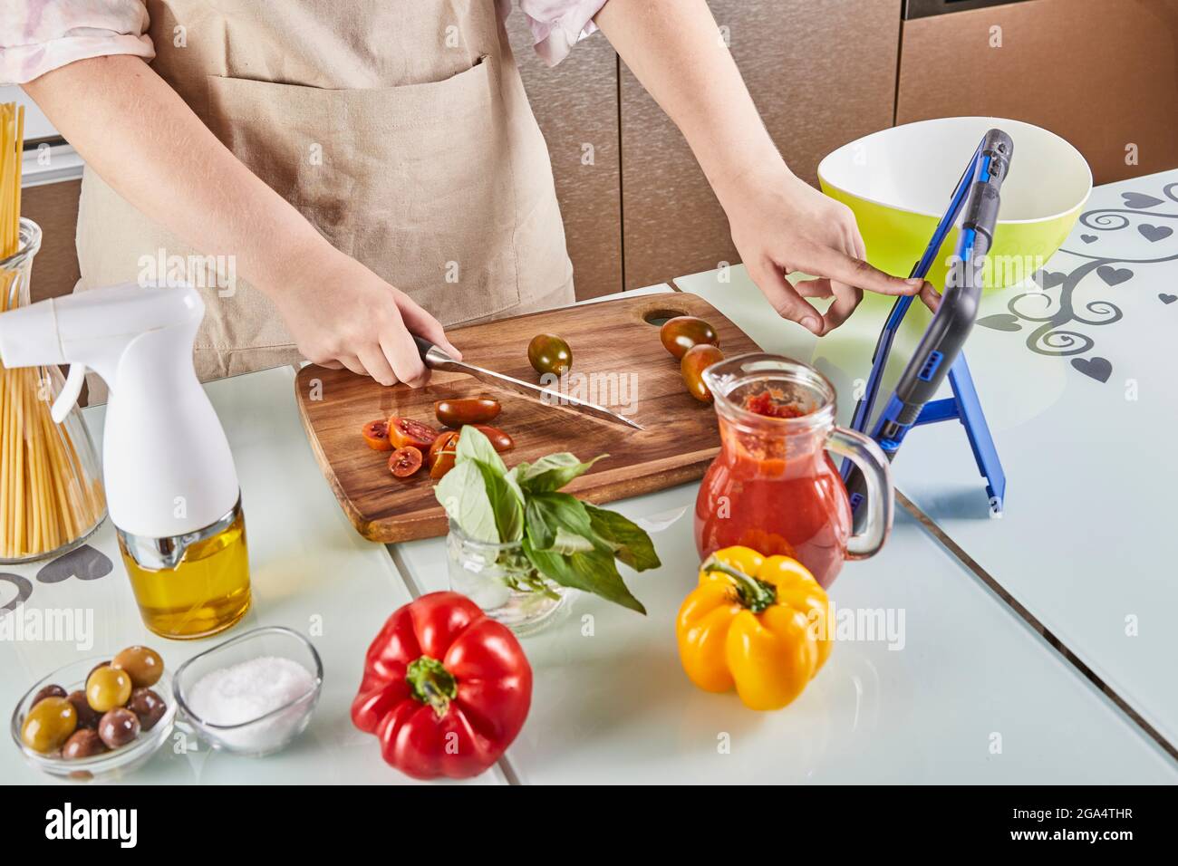 Teenager slides his finger across the tablet screen while cooking through virtual online master class, watches digital recipe while preparing a Stock Photo
