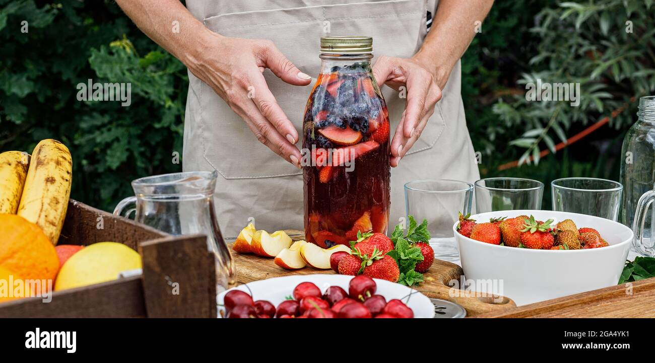 Food banner. Glass bottle with refreshing homemade lemonade or sangria punch with citrus fruits and organic berries. Woman hands hold a summer cocktai Stock Photo