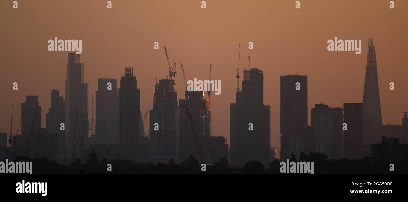 Wimbledon, London, UK. 29 July 2021. Clear and cool sunrise over the London skyline after a previous day of torrential rain showers. Rising sun lights up the eastern faces of skyscrapers under construction near Battersea on the south side of the river Thames and gradually concealing views of the City of London office buildings. Credit: Malcolm Park/Alamy Live News. Stock Photo