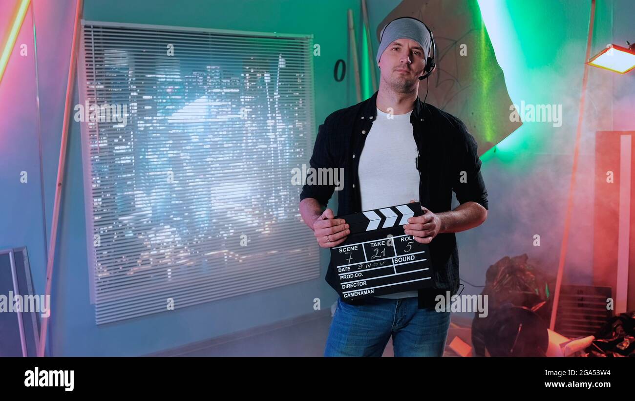 Medium shot of film producer assistant smiling to the camera and giving action with movie clapper board. Stock Photo