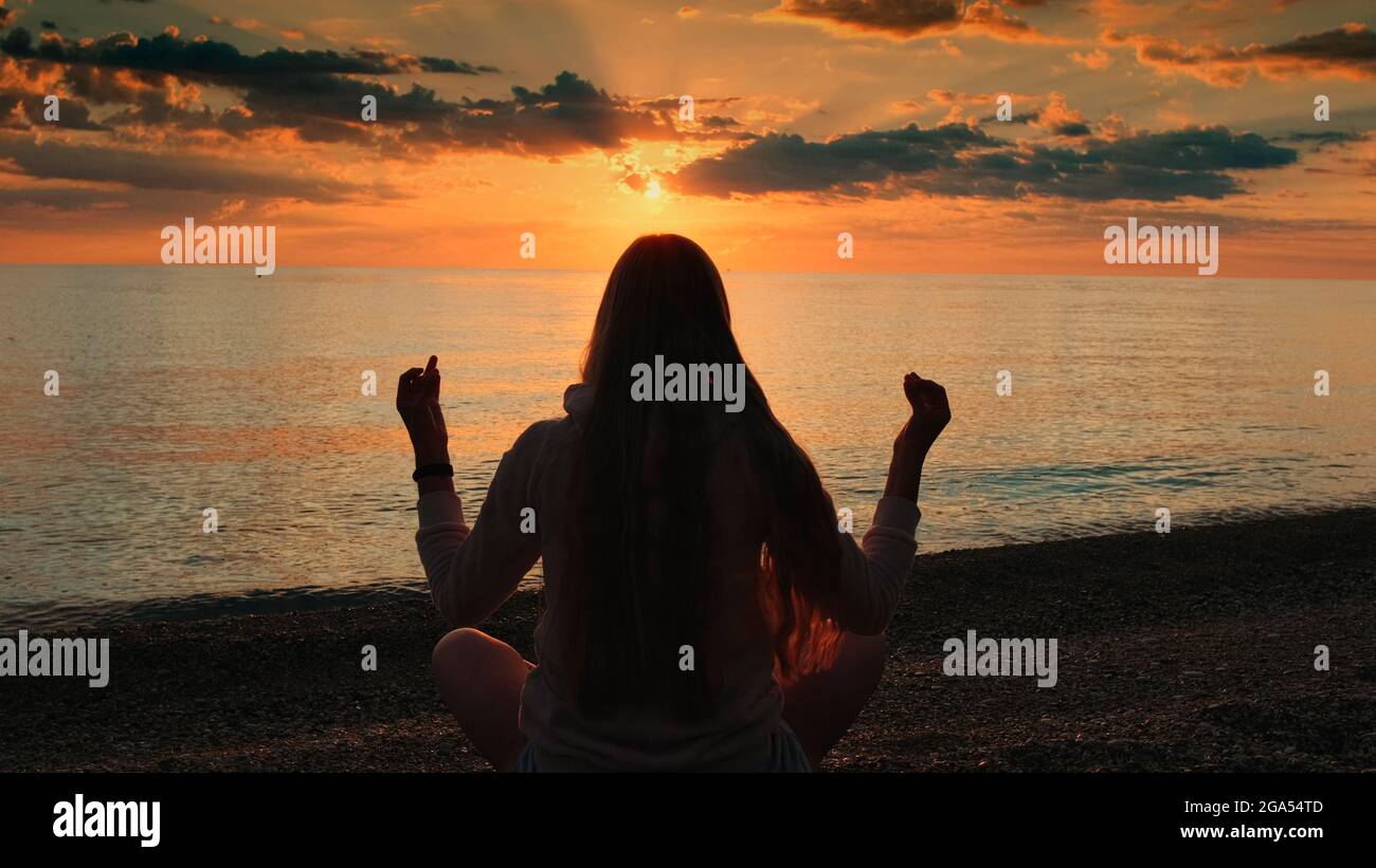 Back view of woman practicing yoga in meditation pose on the beach ...