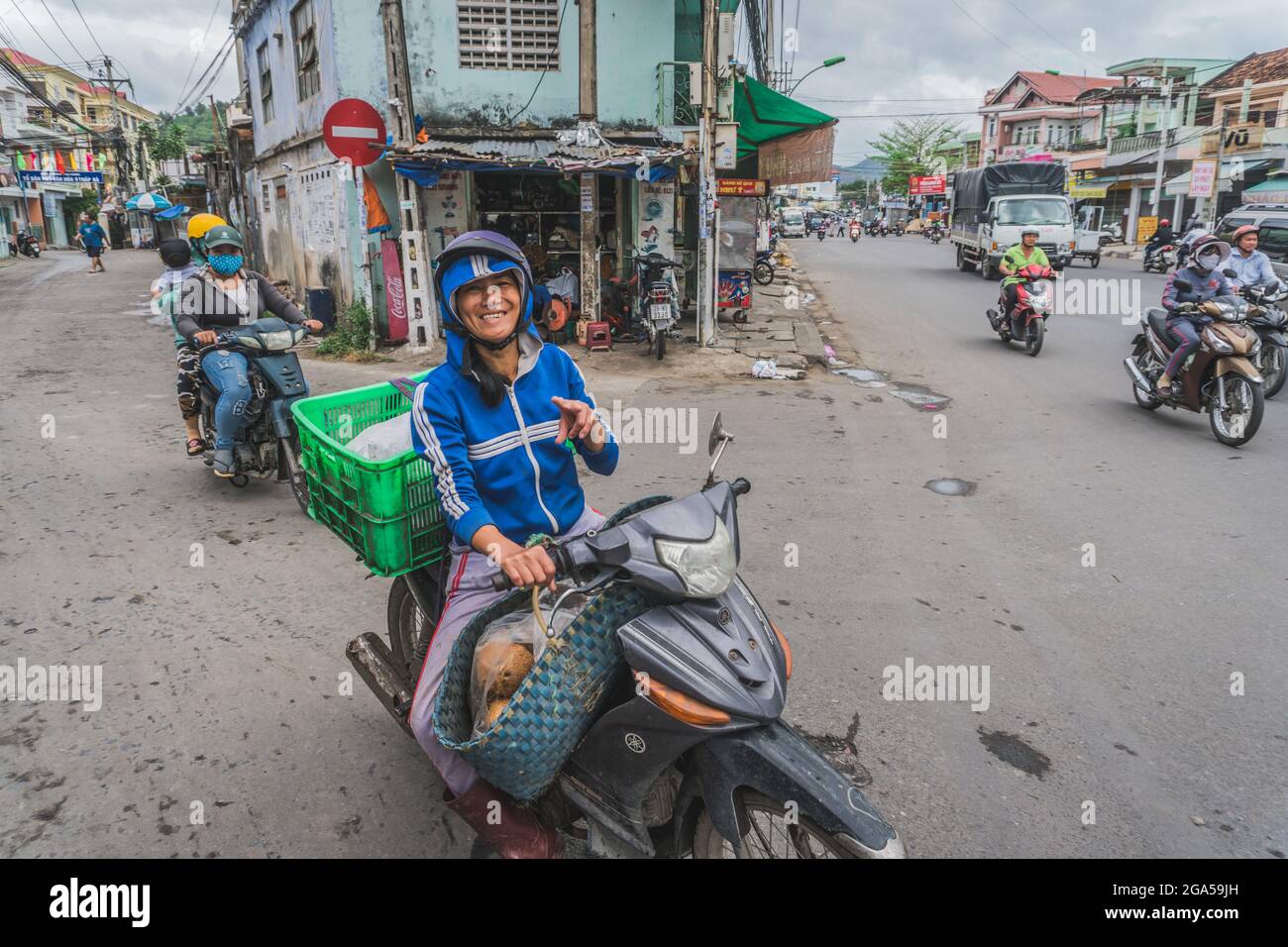 A smiling Vietnamese woman rides a motorcycle and looking at the camera ...
