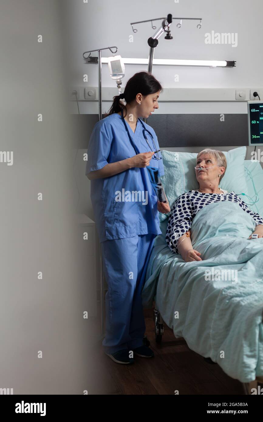 Nurse discussing with elderly patient laying in hospital bed during