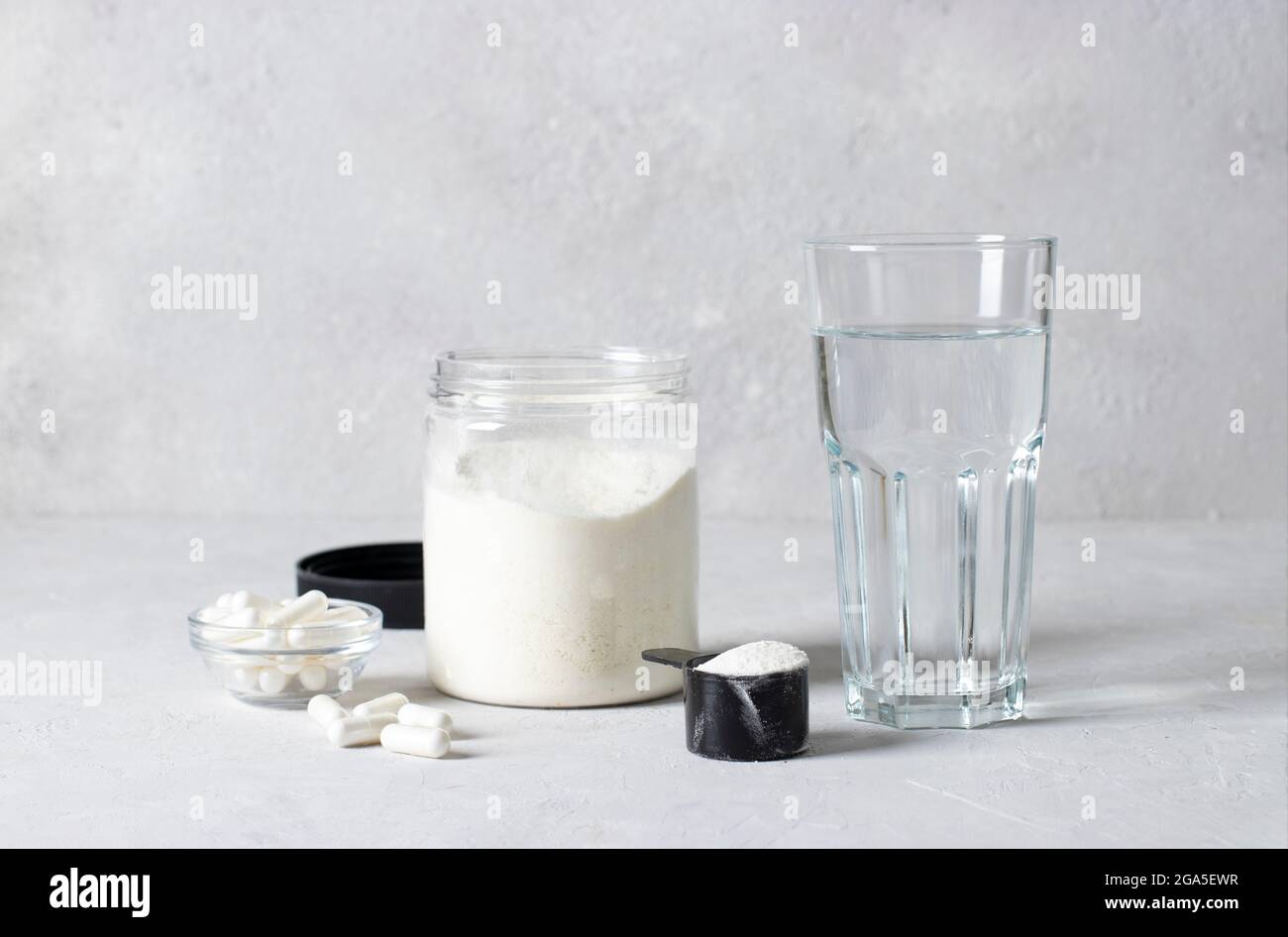 Collagen powder in a jar and measuring spoon, collagen capsules and a glass of water on gray background. Healthy and antiage concept Stock Photo