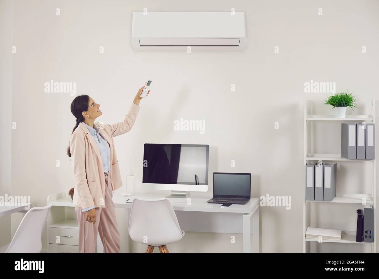 Woman using remote control to switch wall air conditioner in modern office workplace Stock Photo