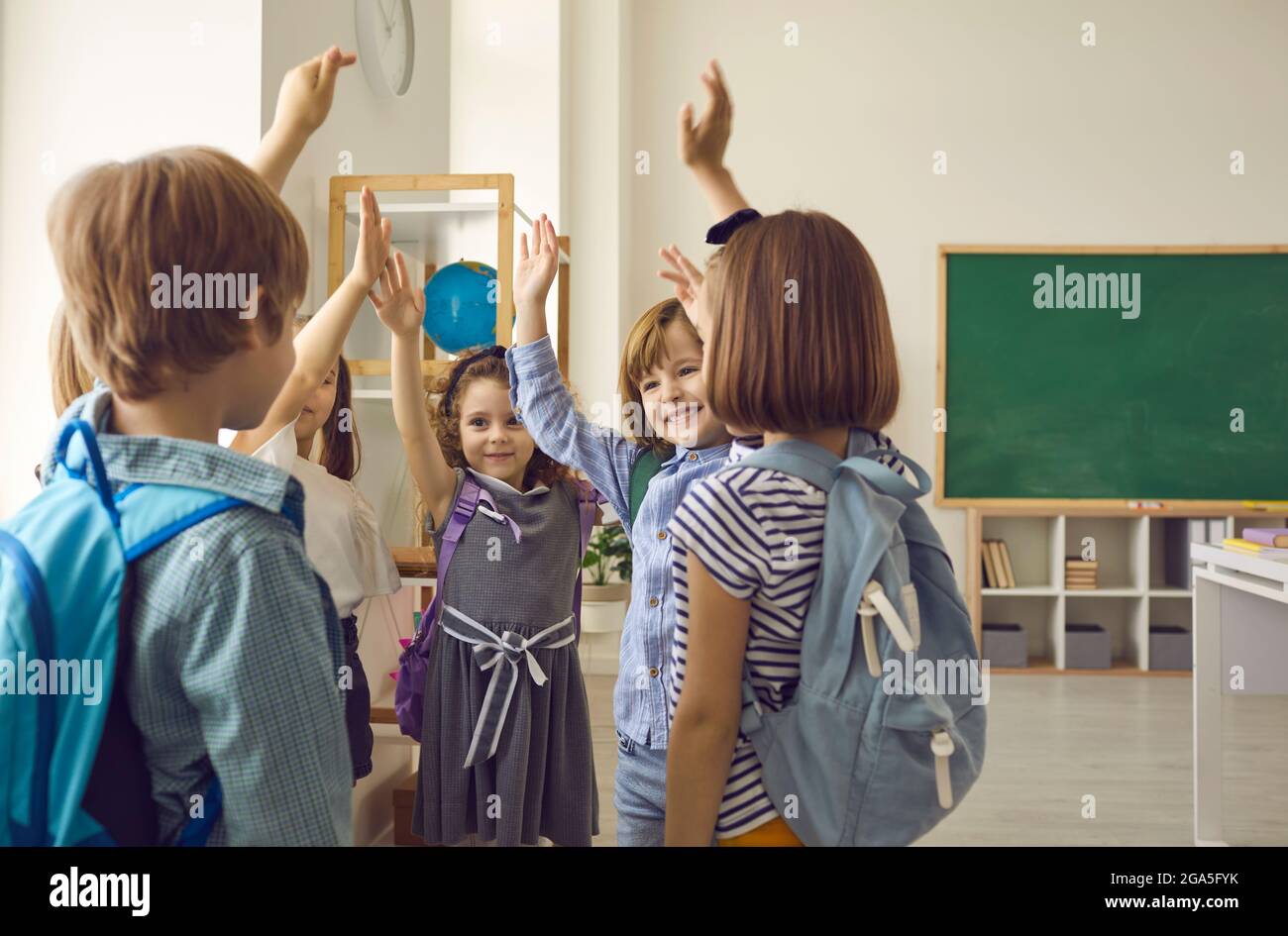 Group of elementary school students stand together raising their hands ...