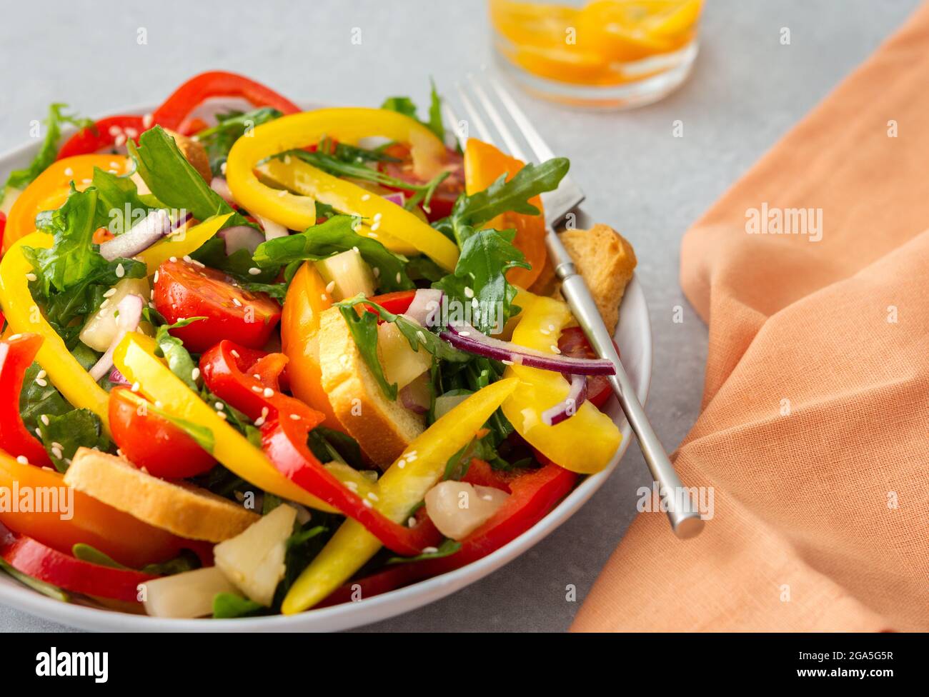 Light summer fresh salad with colorful tomatoes and croutons, sweet peppers and pineapple with sesame seeds, water with kumquats Stock Photo