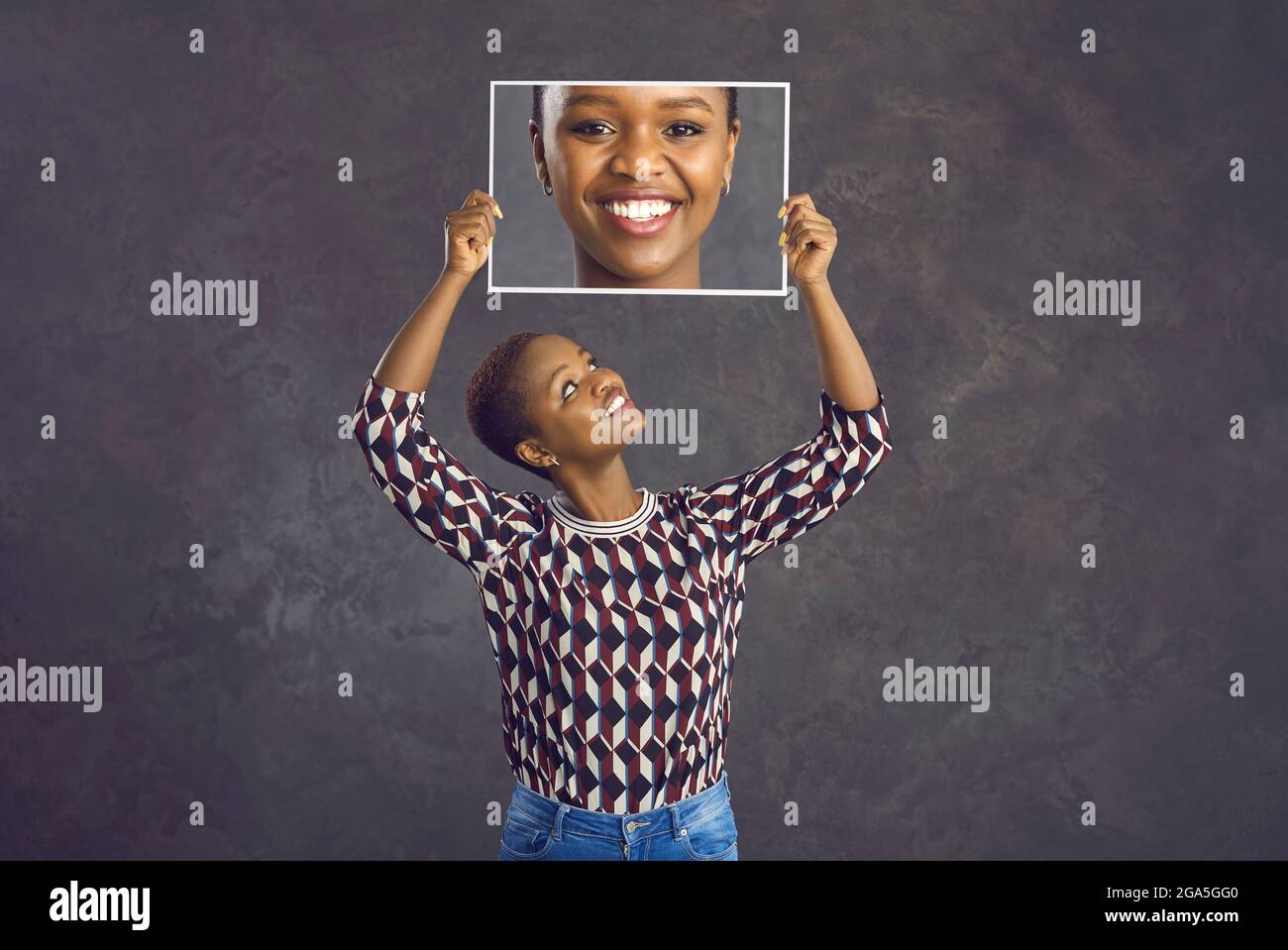 Happy black young woman holding photo of herself standing isolated on grey background Stock Photo