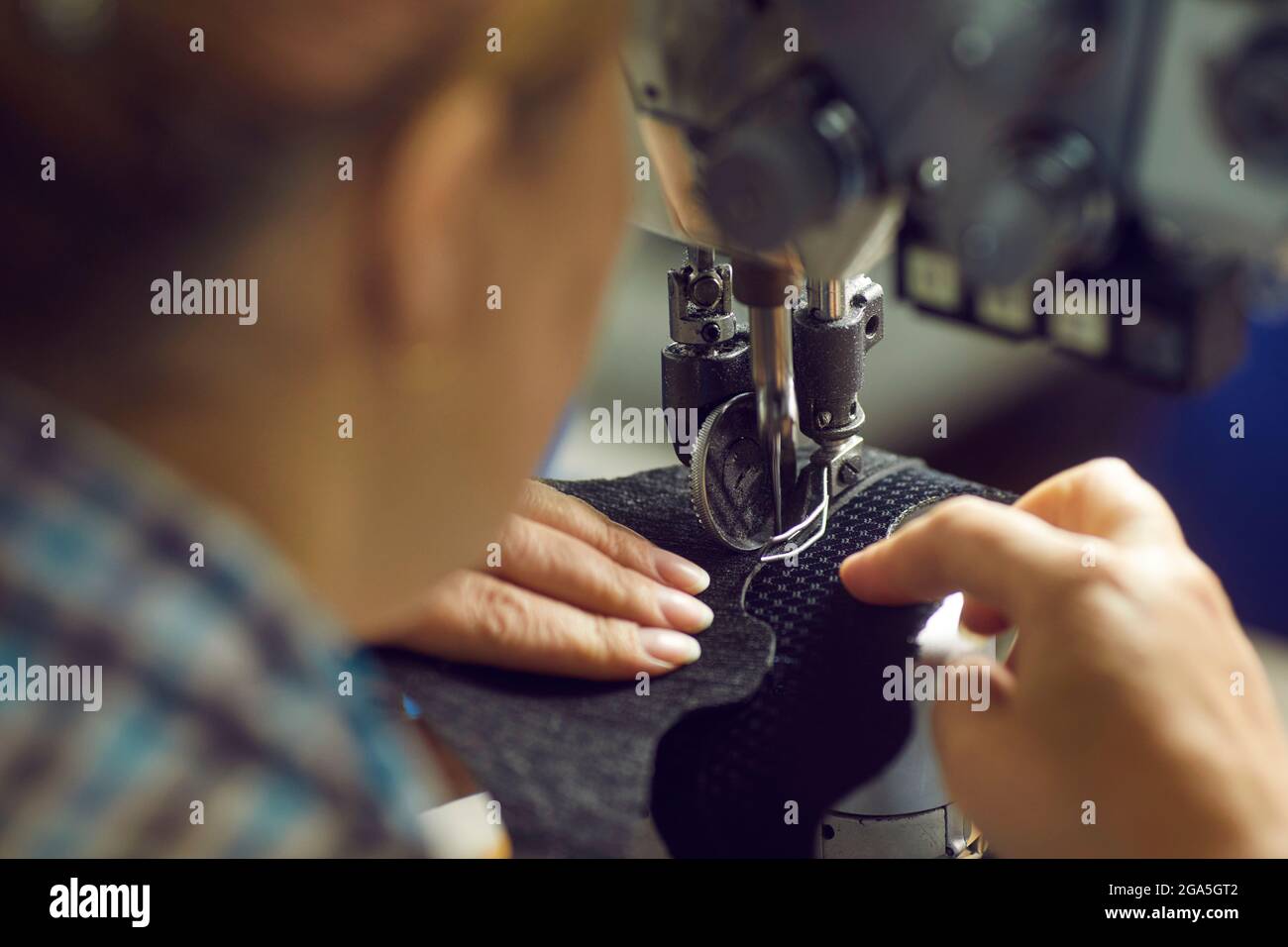 Shoe factory worker making a detail for new footwear on an industrial sewing machine Stock Photo