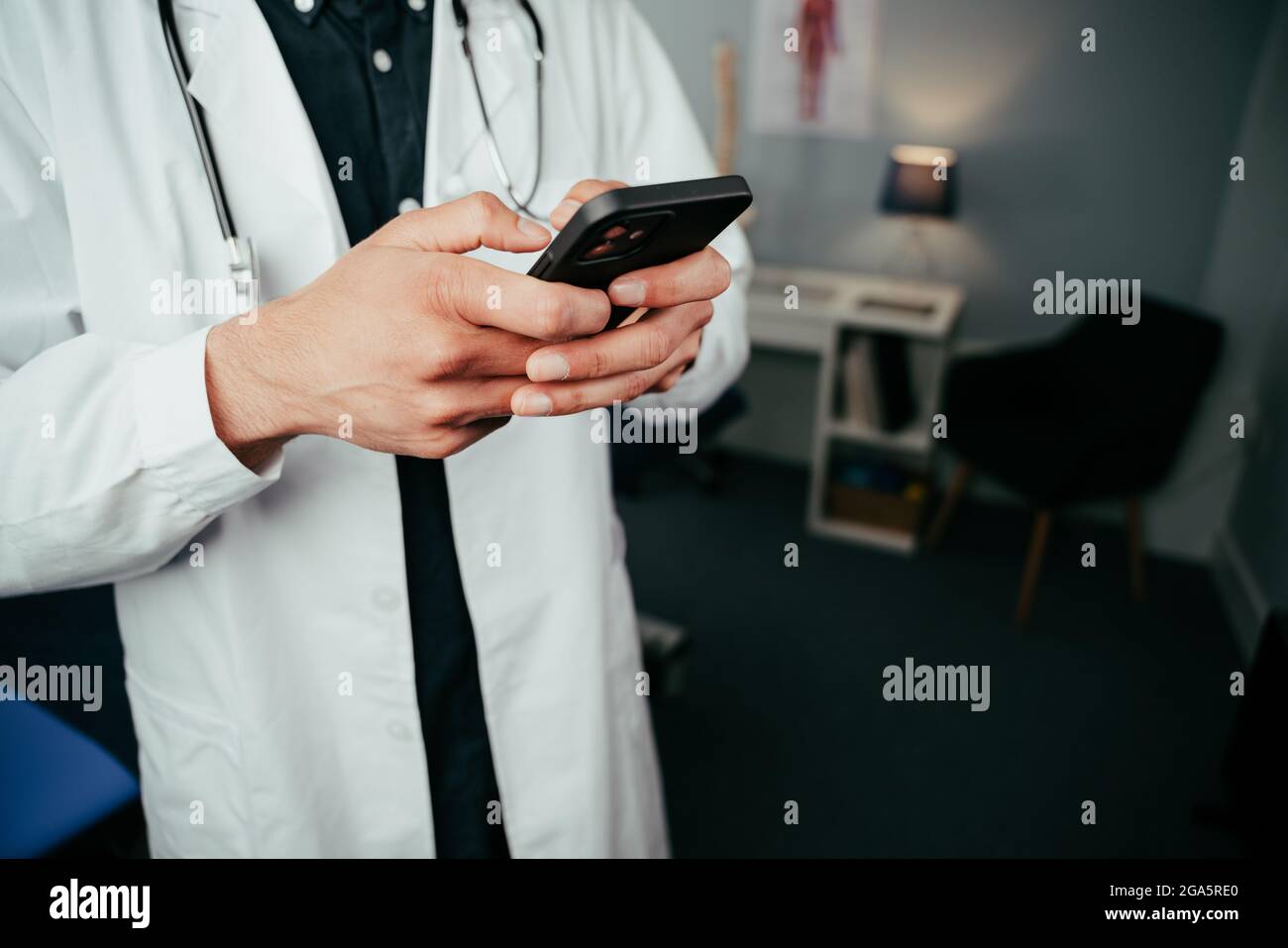 Male doctor standing in clinic typing on cellular device Stock Photo