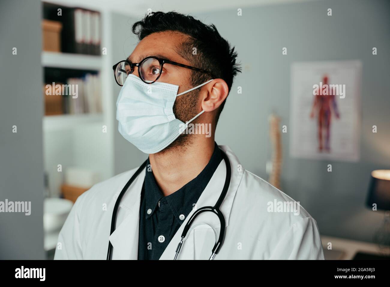 Mixed race male doctor working in clinic wearing surgical mask Stock Photo
