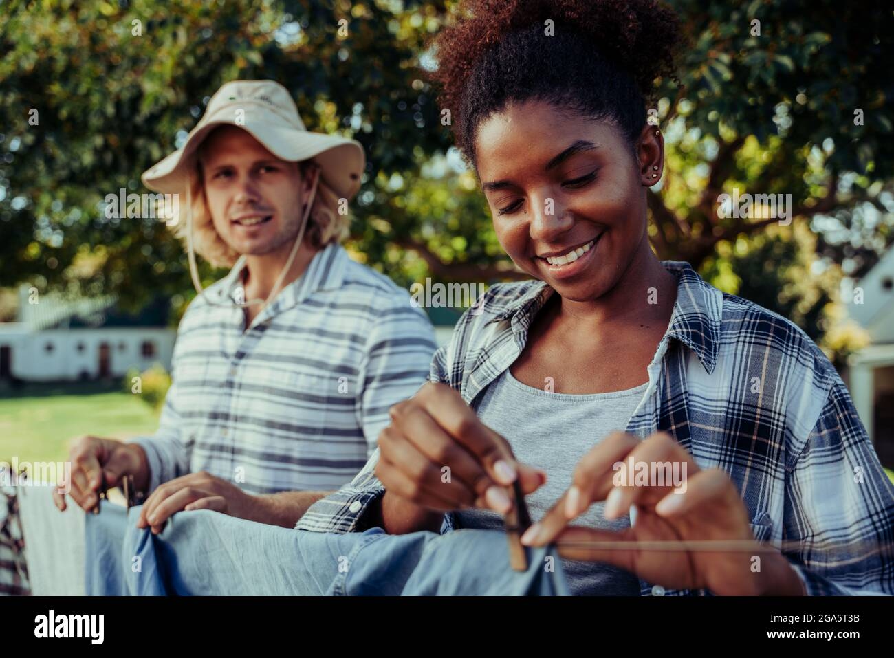 Mixed race female smiling while hanging up clean laundry with caucasian male friend in backyard Stock Photo