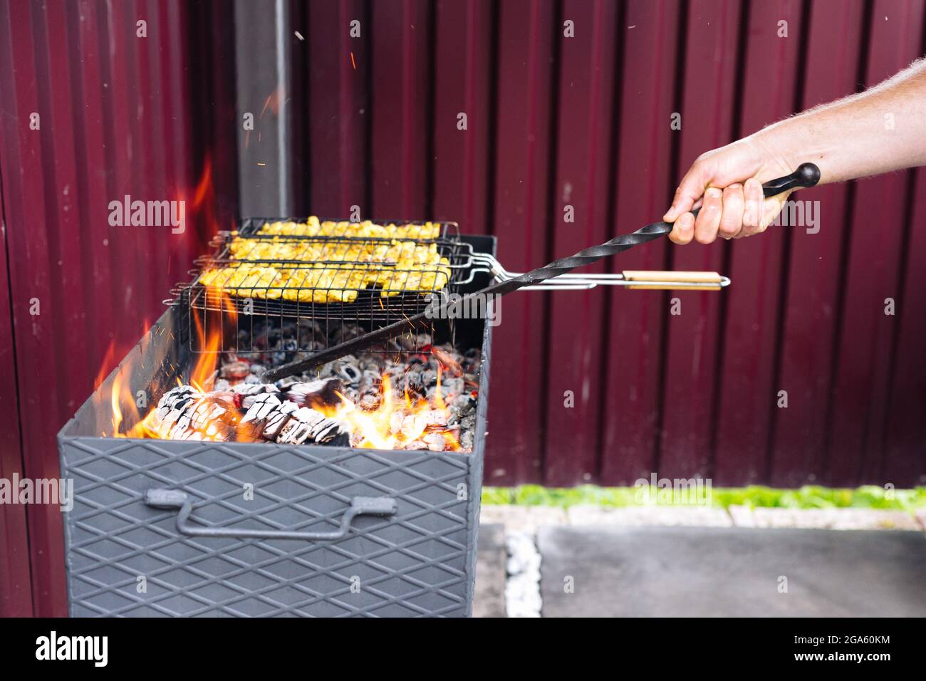 A man using a poker straightens the coals in the grill Stock Photo
