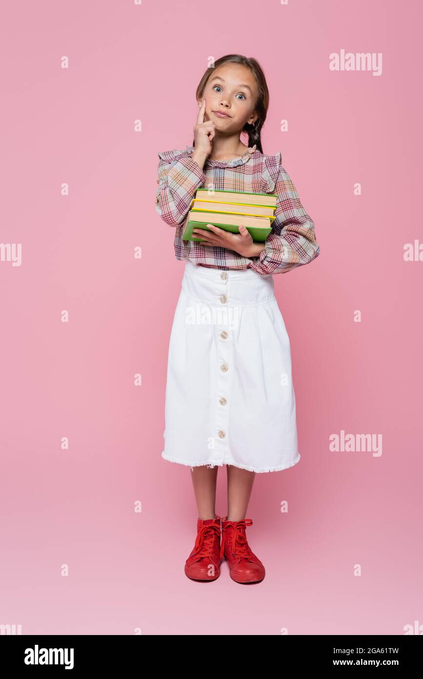 discouraged girl in checkered blouse and white skirt holding books on pink background Stock Photo