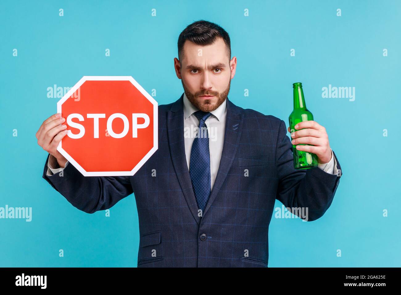 Stop drinking alcohol. Do not drive drunk. Anxious businessman showing alcoholic beverage beer bottle and stop sign, warning and worrying. Indoor stud Stock Photo