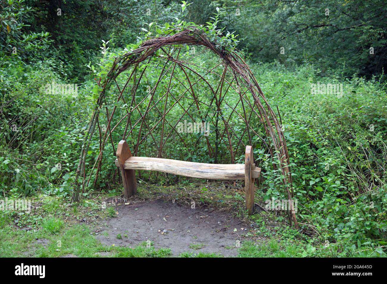 A simple, rustic wooden bench under a lattice wicker domed arch, provided for the public to rest awhile Stock Photo
