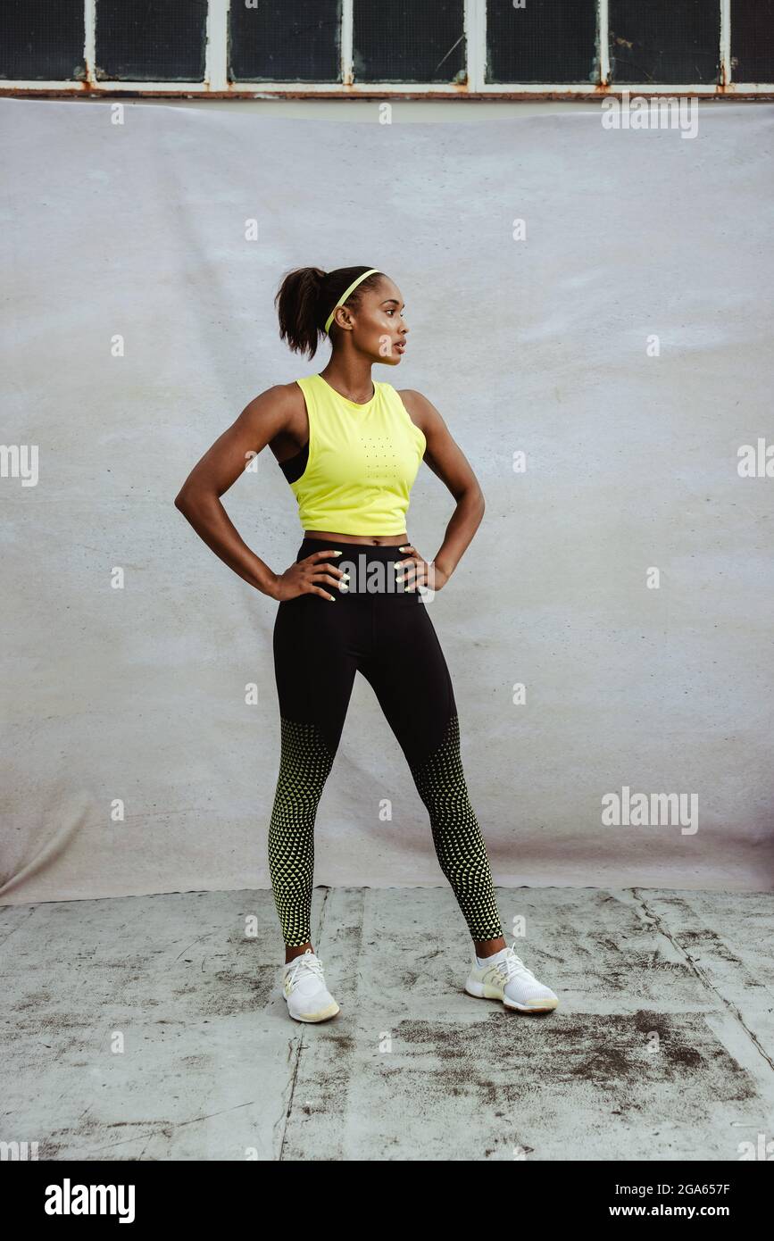 Full length of African woman in sports clothing taking break after workout on a building terrace. Young fitness woman with fit body standing with hand Stock Photo