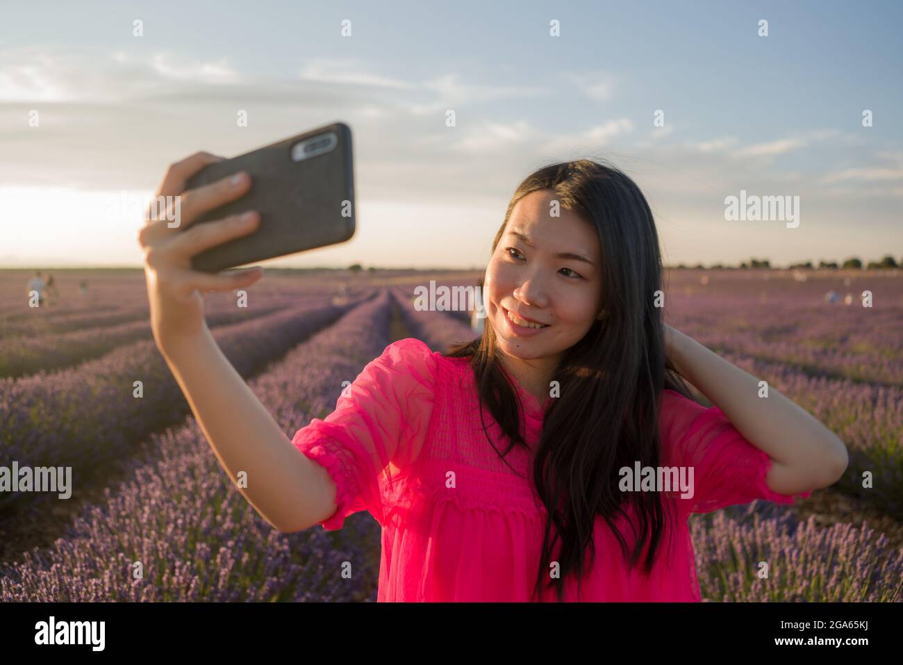 young happy and beautiful Asian Korean woman in Summer dress taking sunset selfie with mobile phone at purple lavender flowers field in nature and rom Stock Photo