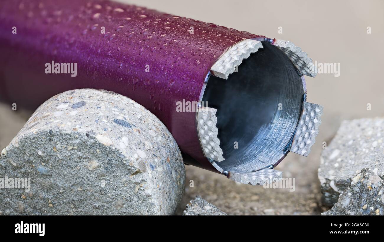 Closeup of wet purple core drill bit. Cylindrical bored piece of gray concrete tile. Drilling hole saw tool - crown of diamond grit. Civil engineering. Stock Photo