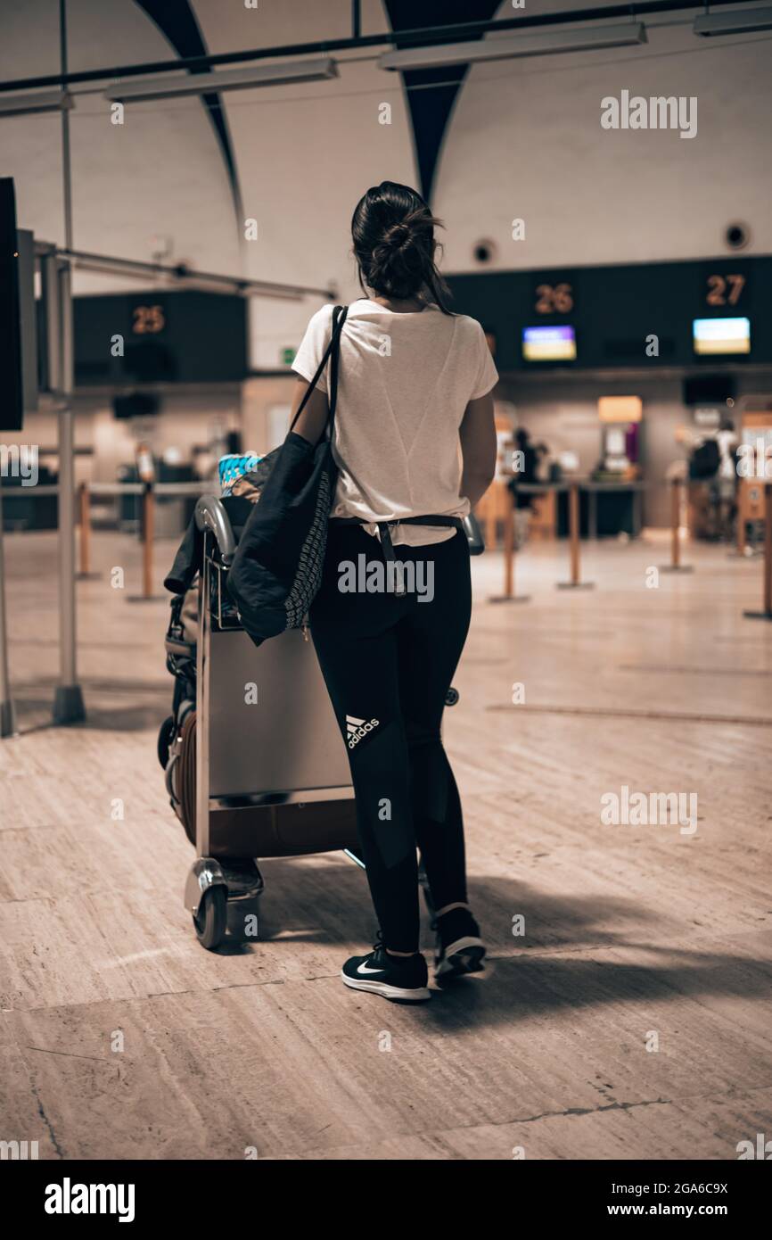 Woman walking through the airport terminal during the covid pandemic loading her luggage into a trolley walking through the terminal corridors Stock Photo