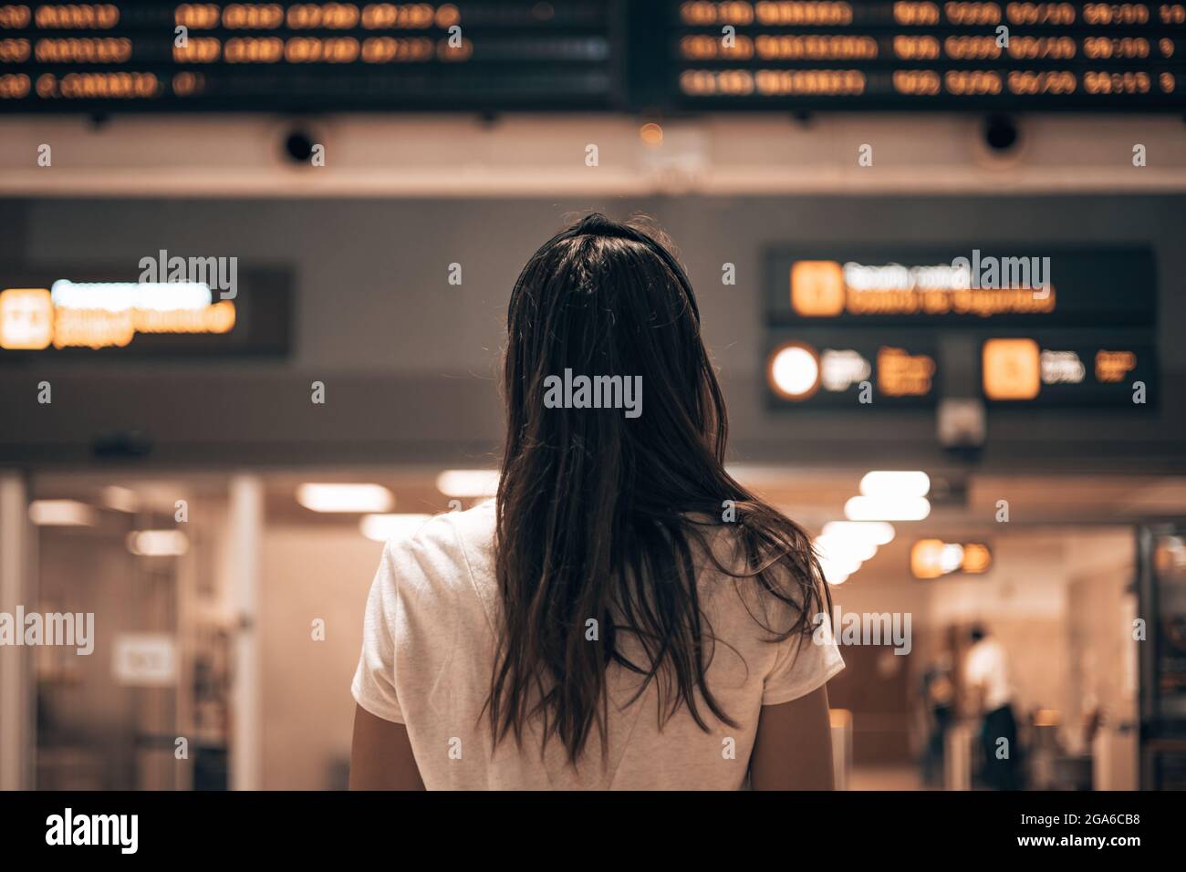 Woman in an airport terminal looking at the large screens showing the departures and arrivals of the planes, waiting for the details of her flight Stock Photo