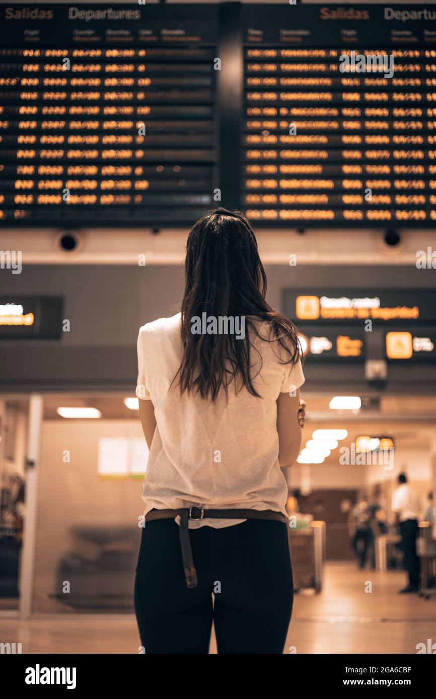 Woman in an airport terminal looking at the large screens showing the departures and arrivals of the planes, waiting for the details of her flight Stock Photo