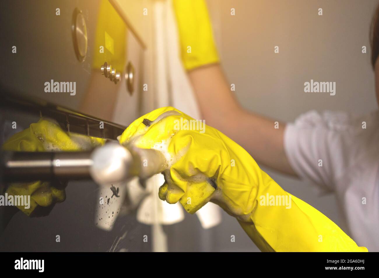 Woman cleaning and wiping the stove door closeup view to hand in yellow