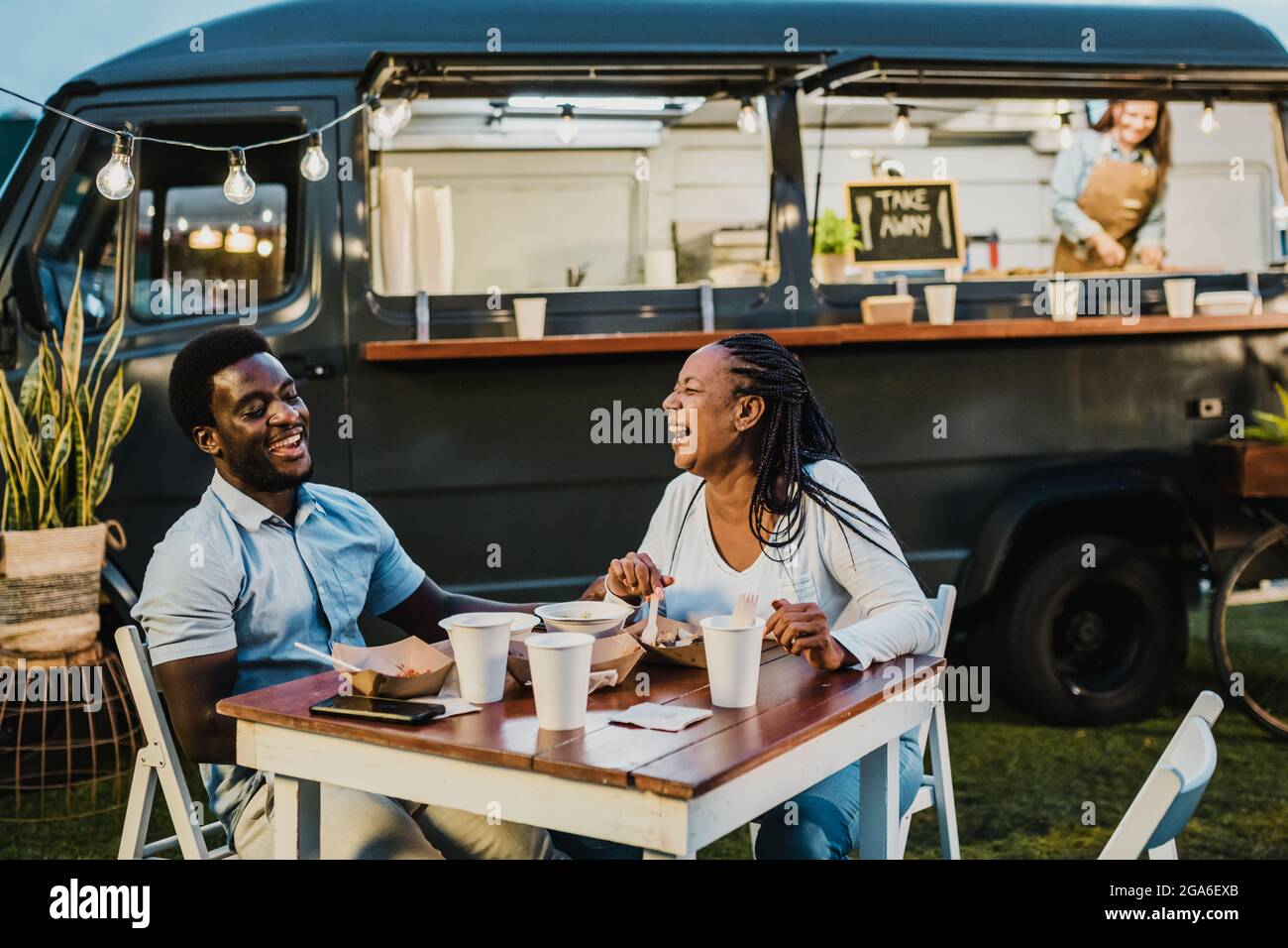 Happy black couple laughing during dinner near food truck Stock Photo