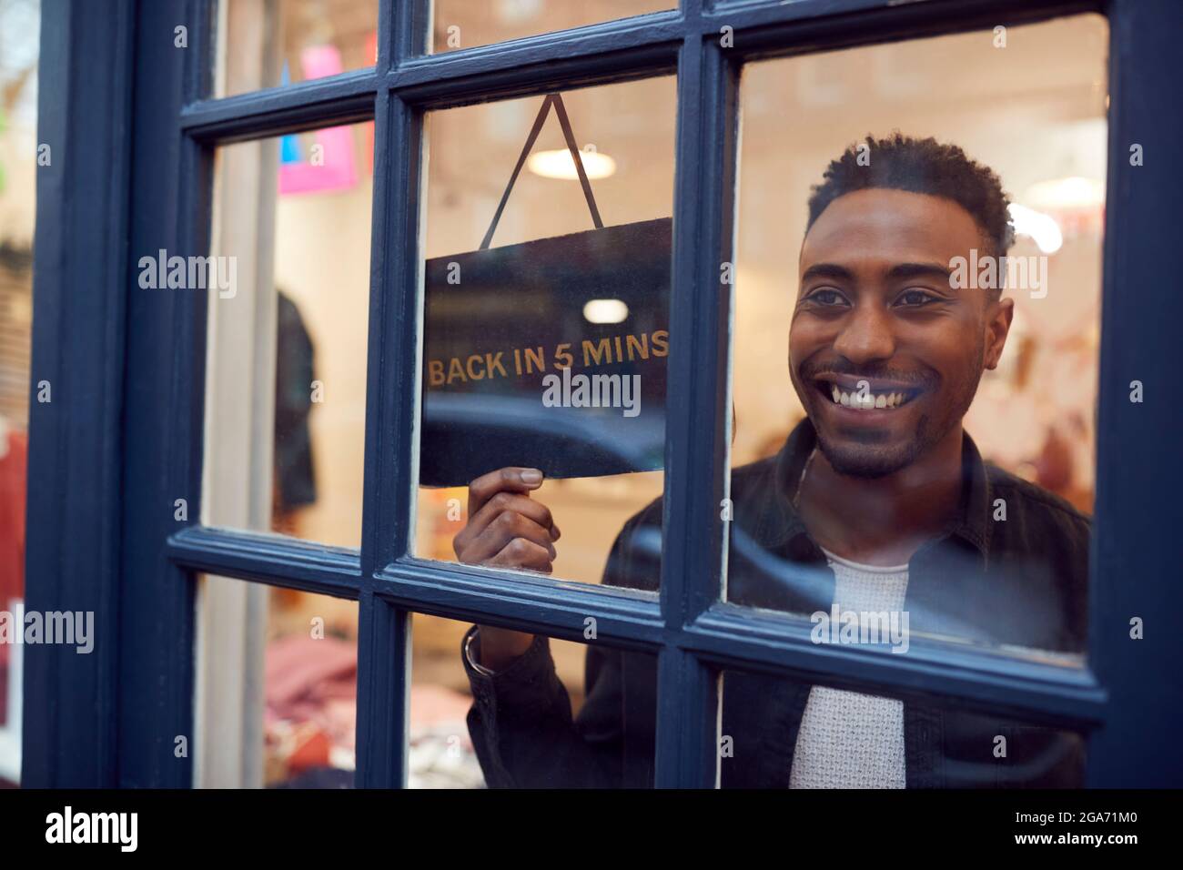 Smiling Small Business Owner Turning Around Back In 5 Minutes Sign On Shop Or Store Door Stock Photo