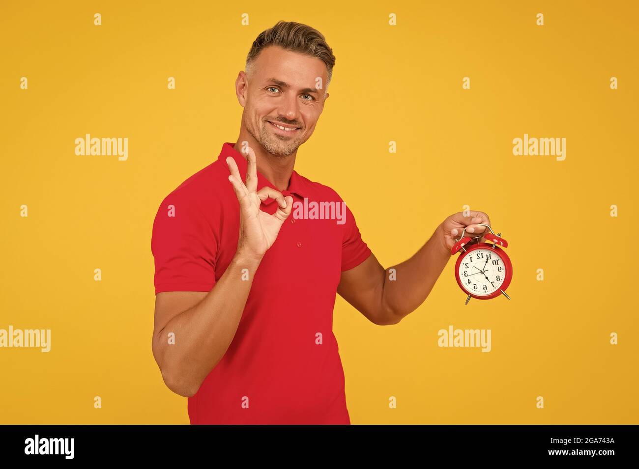 All right. Happy man hold alarm clock showing OK sign. Punctuality and accurate timekeeping. Chronometry and timekeeping. Clock gives the right time Stock Photo