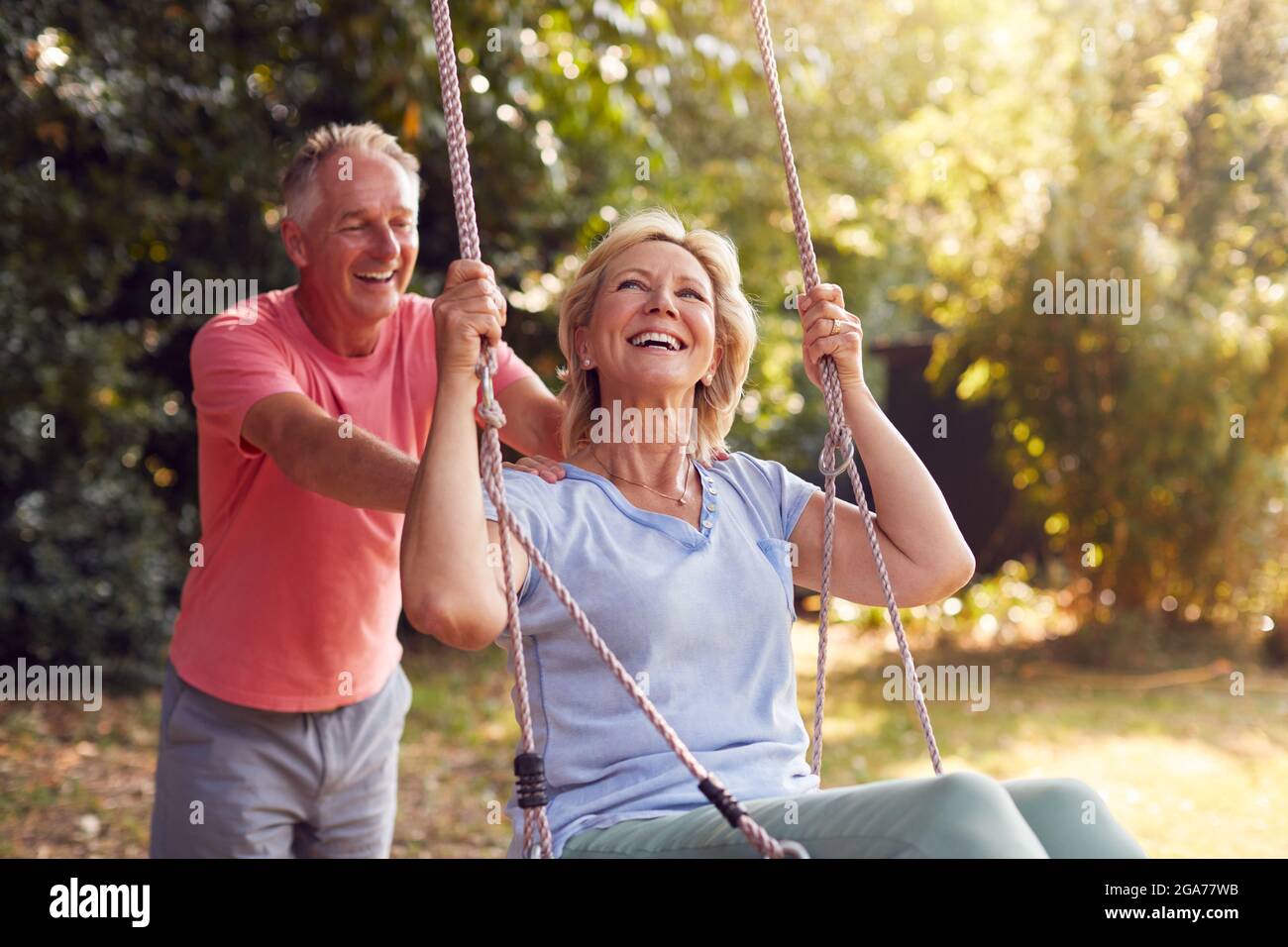 Retired Couple Having Fun With Man Pushing Woman On Garden Swing Stock Photo