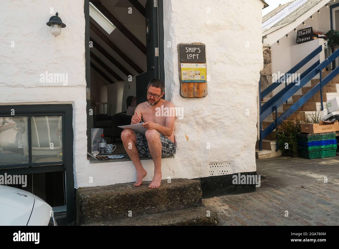 An artist sat on his doorstep drawing in St Ives Cornwall Stock Photo