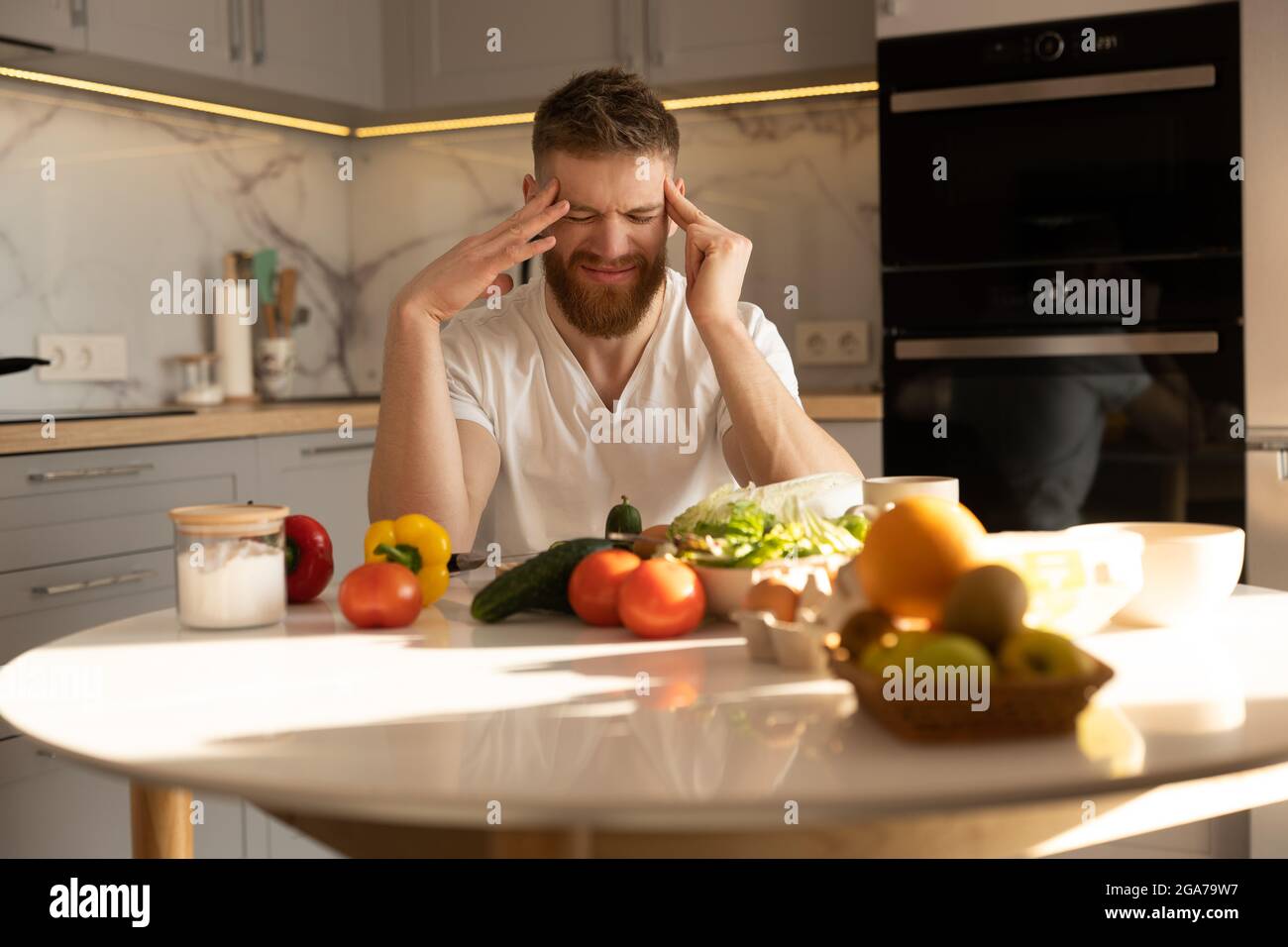 Young tired man with headache sitting at table Stock Photo