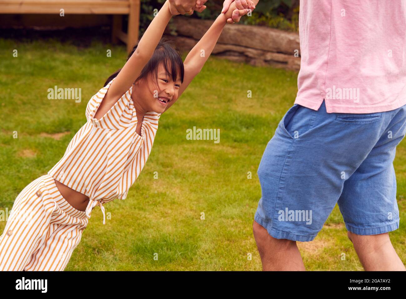 Asian Father Swinging Daughter By Arms As They Play Game In Garden Together Stock Photo