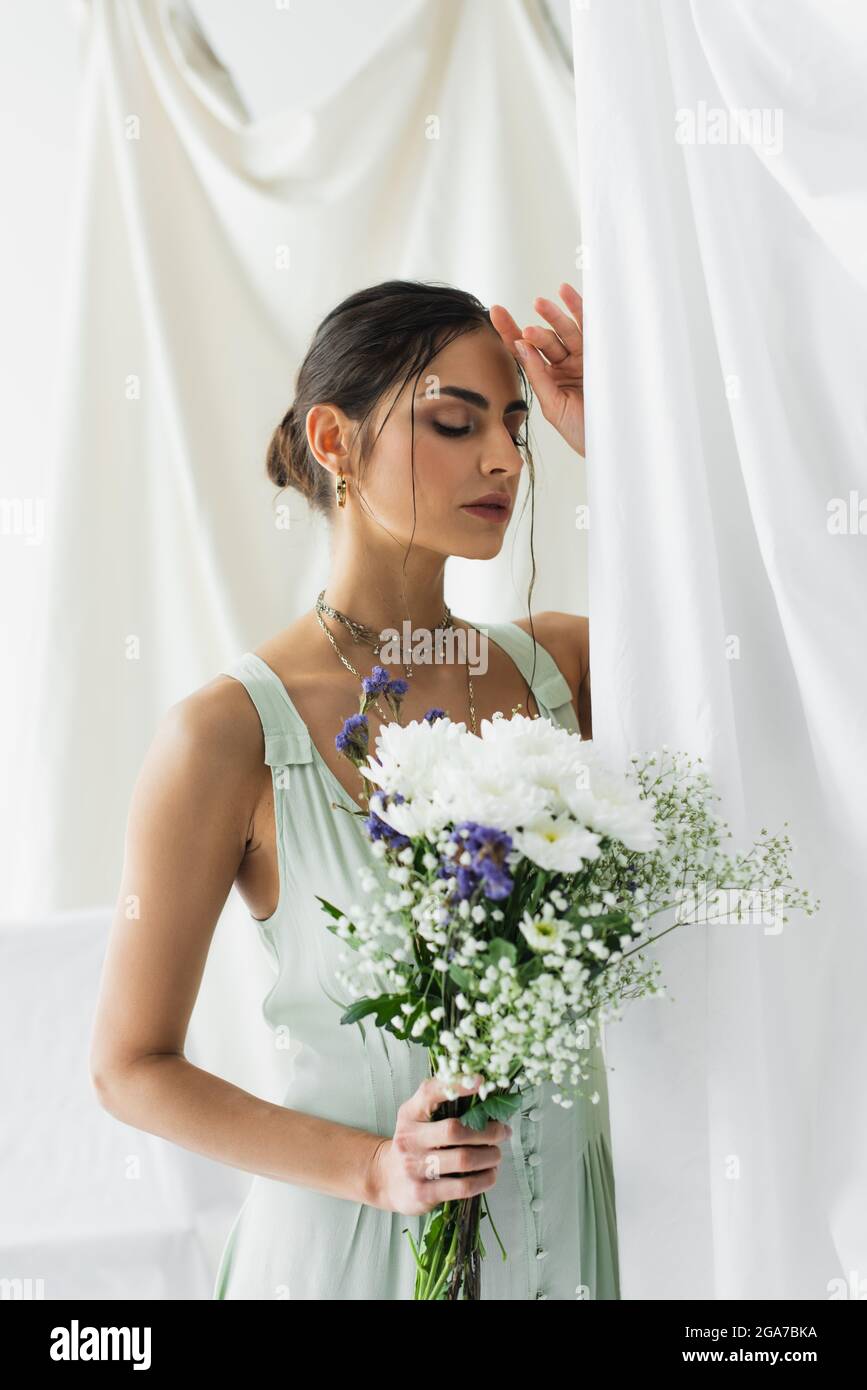brunette woman in dress posing with bouquet of flowers on white Stock ...
