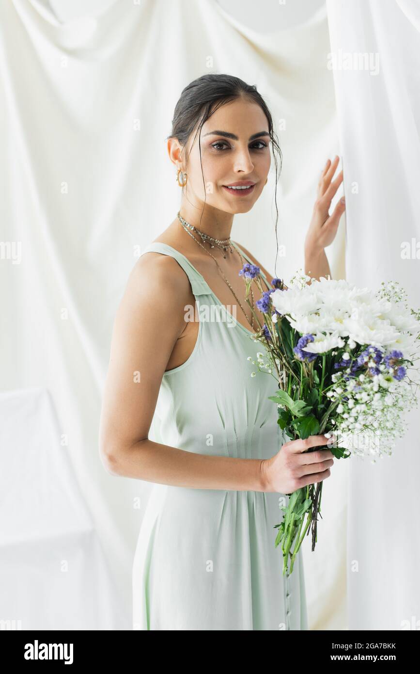 cheerful woman in dress holding bouquet of flowers on white Stock Photo ...