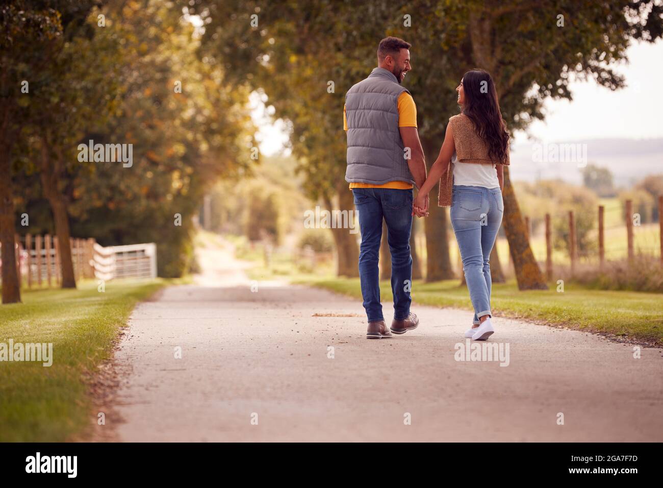 Rear View Of Loving Couple Walking Hand In Hand Along Track Through ...