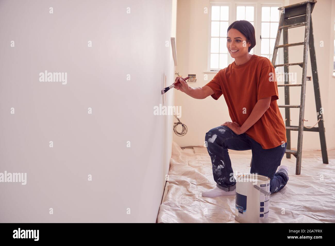 Woman Painting Test Squares On Wall As She Decorates Room In New Home
