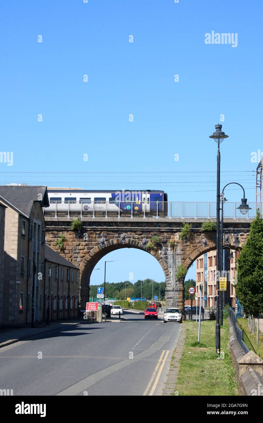 View along St Georges Quay in Lancaster, Lancashire, England to a Northern trains diesel multiple unit crossing Carlisle Bridge on 17th July 2021. Stock Photo