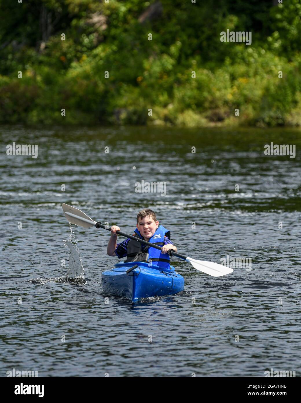 Boy kayaking in Adirondack State Park New York State New England boy in blue kayak wearing a lifejacket lifevest / life jacket or life vest Stock Photo