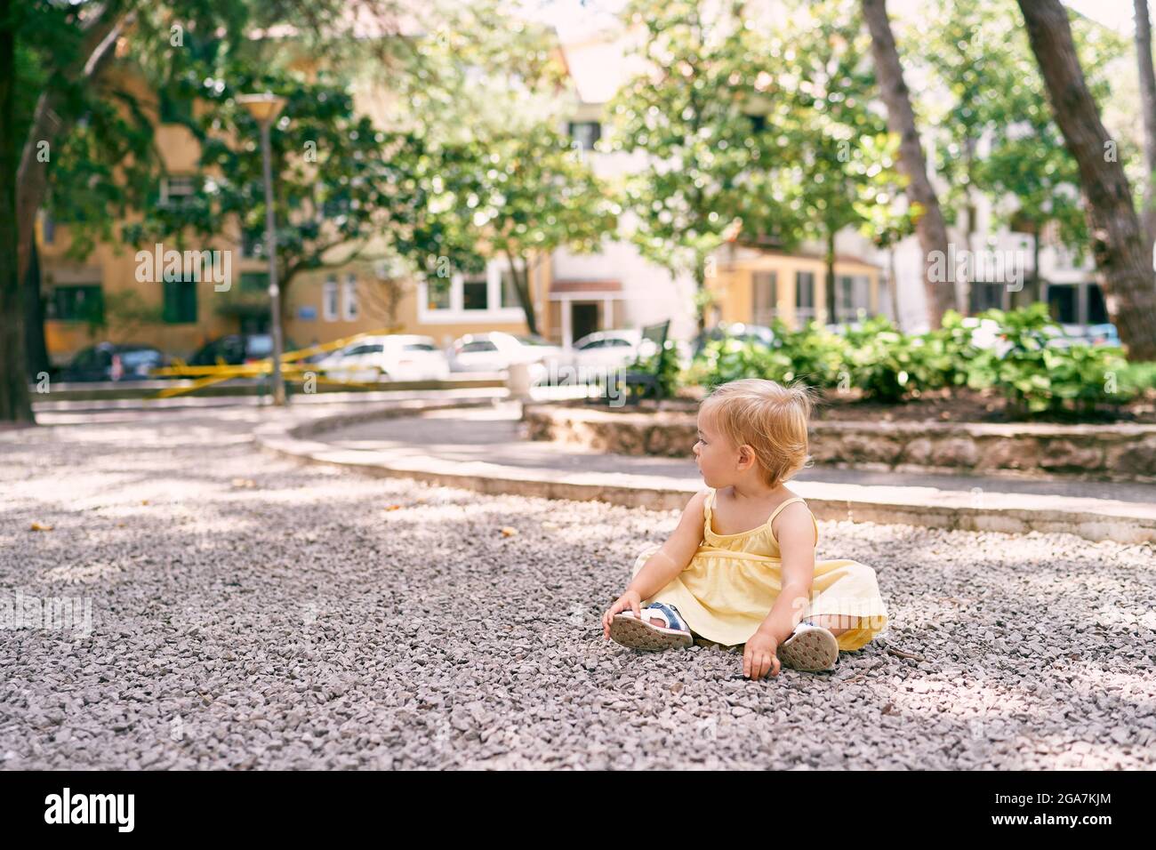 Little girl in a dress sits on a gravel path in the courtyard of the ...
